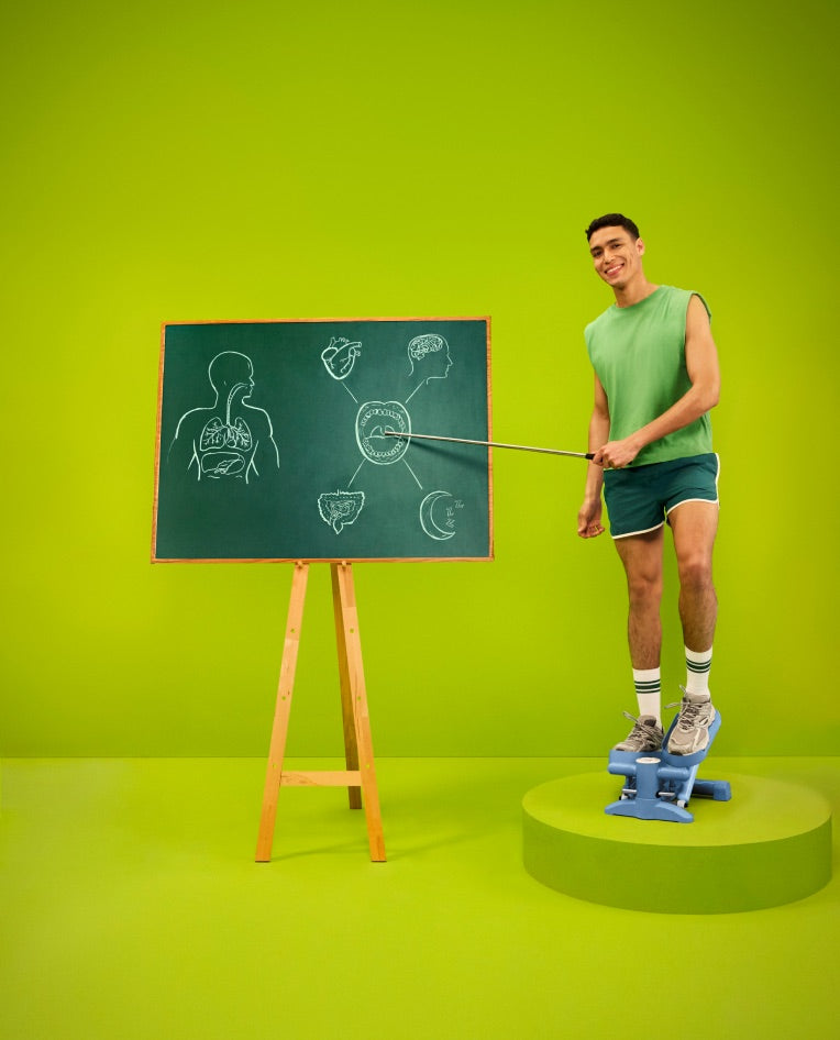 A man in sportswear pointing at a chalkboard diagram of the body