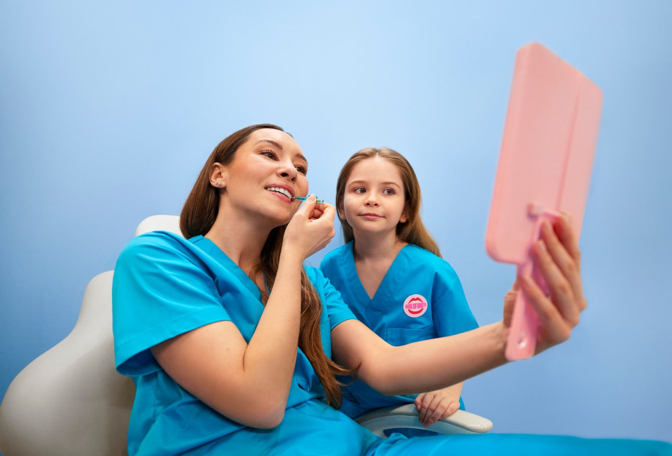A dental hygienist showing a young girl how to brush, holding up a mirror